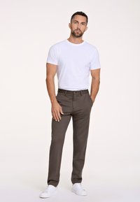 Herrenoutfit mit einem taillierten weißen Baumwoll-T-Shirt und dunkelgrauen Baumwollhosen. Kombiniert mit weißen Sneakern, zeigt es einen einfachen, modernen Stil.