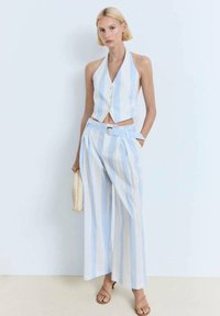 Svijetloplava i bijela prugasta halter majica s prednjim gumbima, u kombinaciji s širokim prugastim hlačama i odgovarajućim remenom. Pleteni dodatak torba.