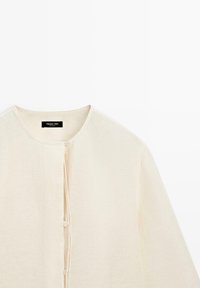 Kremowy lekki kardigan z długim rękawem, okrągłym dekoltem i trzema małymi guzikami z przodu, metka z napisem Massimo Dutti.