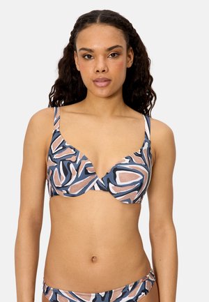 Mujer con cabello rizado que lleva un bikini con un patrón abstracto en azul, rosa y blanco, tanto en la parte superior como en la inferior, sobre un fondo claro y liso.