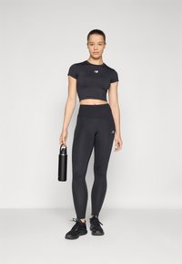 Mustem sportlik komplekt, mis koosneb lühikestest varrukatest cropped-särgid ja kõrge vöökohaga retuusidest, millele on lisatud must veepudel ja spordijalatsid.