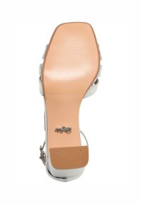 Sandalía blanca de tacón alto con parte superior de cuero sintético suave. La suela es de color tostado con textura estriada e incluye un logo plateado. Talla 38 marcada.