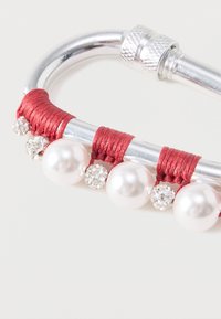 Punase niidiga kaetud metallist karabiin hõbedaste detailide ja suurte valgete pärlitega, kaunistatud lisadetailide jaoks läbipaistvate rhinestone'idega.