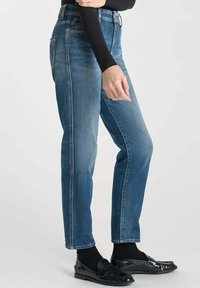 Blauwe denim straight-leg jeans met een vervaagde afwerking, vijf zakken en riemlussen; gecombineerd met zwarte schoenen en sokken.
