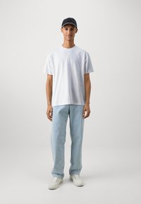 Tricou alb cu mânecă scurtă și guler rotund, blugi lejerați de culoare albastră deschis, și adidași albi. Căciulă neagră cu un model texturat.