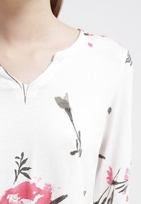 Vit topp med v-ringning som har ett blommönster i rosa och grått. Mjuk tyg med korta ärmar och en avslappnad passform. Subtila sömnadsdetaljer.