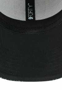 Innenansicht einer schwarzen Stoffmütze mit sichtbaren Nähten und einem vertikalen Etikett mit der Aufschrift "9FORTY" auf einem grauen Netzkronenpanel.