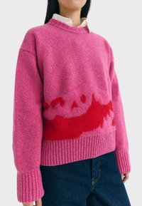 Fuchsia pink uldtrøje med et rødt abstrakt mønster. Ribbet manchet og kant, rund halsudskæring. Struktureret overflade. Sammenstylet med mørke denimbukser.