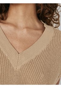 Krémový pletený svetr s véčkovým výstřihem a žebrovanými okraji, s texturovaným povrchem a otevřeným vzorem.