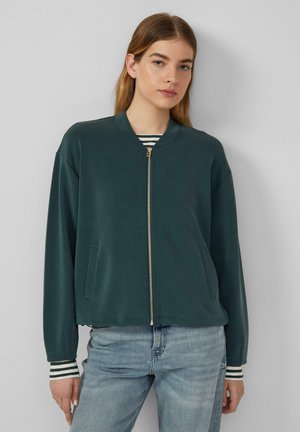 Giacca bomber verde scuro con zip anteriore, tasche laterali e polsini a righe. Realizzata in tessuto morbido, presenta una vestibilità rilassata.