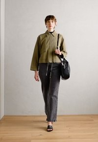 Olivengrønn kort jakke med krage, sammen med grå rette jeans og svarte glidede sandaler, bærende en svart teksturert håndveske.