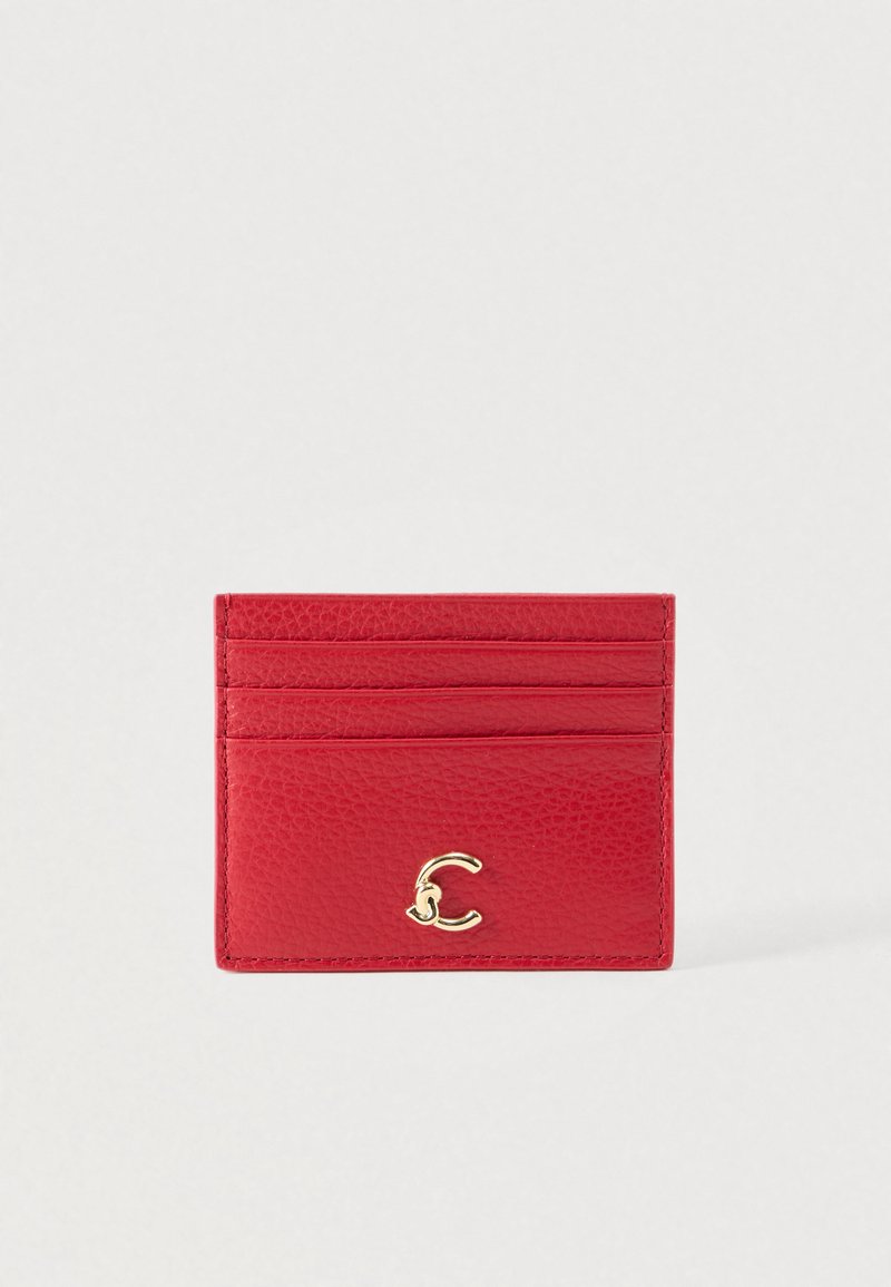 Porte-cartes en cuir rouge avec quatre fentes pour cartes et un petit fermoir doré courbé à l'avant, sur un fond clair et uni.