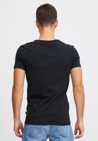 T-shirt nera in cotone con design aderente, maniche corte e scollo rotondo, vista da dietro, con una texture liscia.