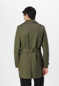 Trench coat verde oliva con cintura ceñida, hombreras y espalda ventilada. Confeccionado en una tela suave y duradera.