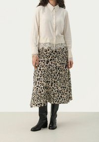 Cremefarvet skjorte med knaplukning og blonder, sammen med en luftig nederdel med leopardprint. Sorte knæhøje støvler fuldender outfittet.