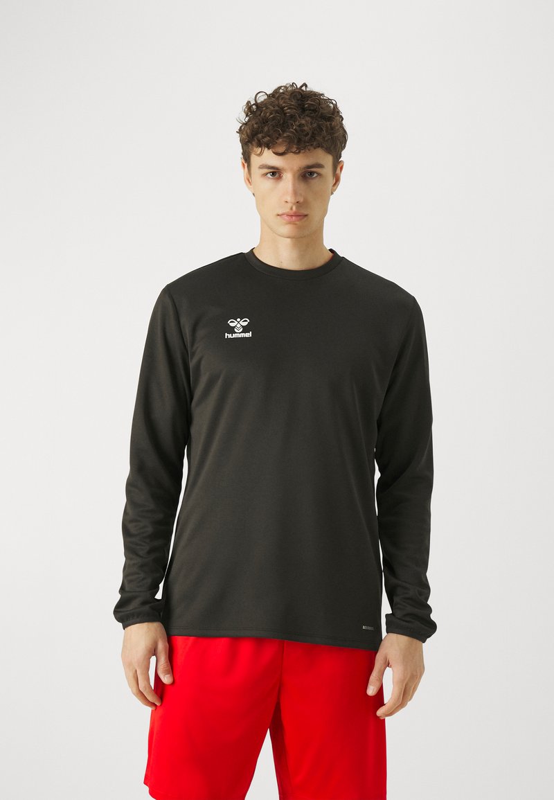 Langärmliges schwarzes Sportshirt aus leichtem, glattem Stoff, mit einem Logo auf der Brust und einem Rundhalsausschnitt. Kombiniert mit roten Shorts.