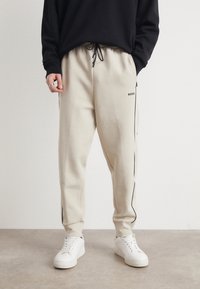 Beige sweatpants med sort sidepiping, elastisk talje og justerbar snor. Sæt sammen med hvide sneakers. BOSS-logo på låret.