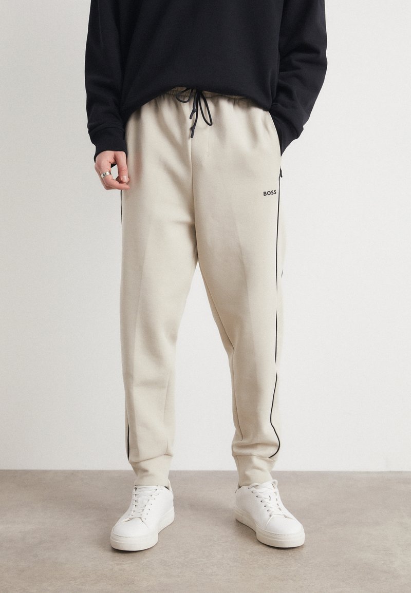 Beige sweatpants med sort sidepiping, elastisk talje og justerbar snor. Sæt sammen med hvide sneakers. BOSS-logo på låret.
