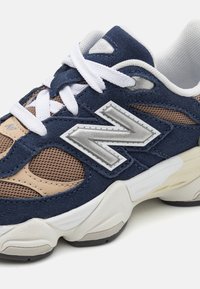 Sneaker in suede blu navy con pannelli in rete beige, lacci bianchi, dettagli in logo argento e suola in gomma testurizzata. Regolabile per un maggiore comfort.