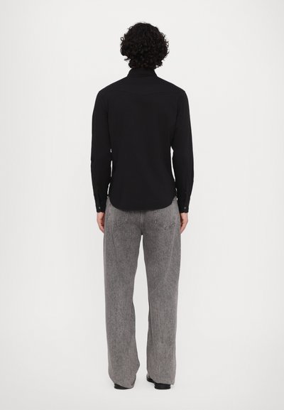 Cămașă neagră cu mânecă lungă, cu guler, ajustată pe corp, asortată cu o pereche de pantaloni largi gri, cu buzunare la spate și un design texturat.