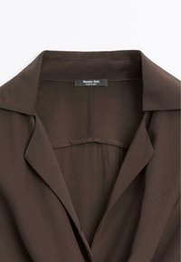 Col et revers de blazer marron foncé avec une étiquette de la marque Massimo Dutti indiquant fabriqué en Chine.