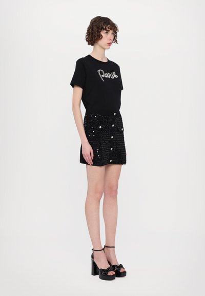 Svart kortärmad T-shirt med "Paris" i silverdetaljer, tillsammans med en svart paljettminikjol med framfickor och knappstängning.