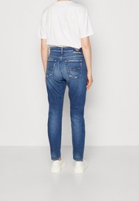 Slim-fit farkut sinisessä denim-kankaassa, joissa on kaksi takataskua, kevyttä kulutusta ja korkea vyötärödesign. Yhdistetty yksinkertaisen valkoisen t-paidan ja valkoisten kenkien kanssa.