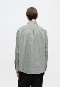 Camisa a rayas con rayas verticales en blanco y negro, de manga larga, con yugo en la parte posterior y puños abotonados. Textura de tela suave.