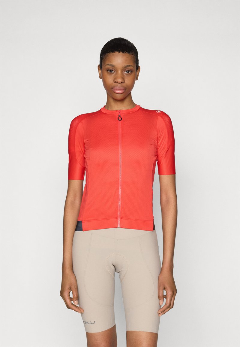 Jersey de ciclismo rojo de manga corta, con cierre de cremallera en el frontal, de tejido texturizado, acompañado de pantalones cortos acolchados beige. Logotipo de marca notable en el hombro.