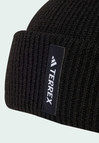 Black knit beanie with ribbed texture and a flat brim. Features a rectangular fabric tag with the brand "TERREX" in white text and logo.