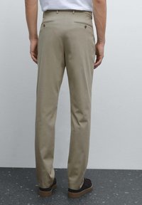 Beige byxor i mjukt tyg, med två bakfickor med knappstängning och rak benvidd, i kombination med mörka skor.