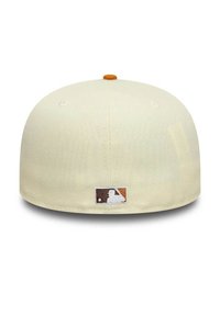 Gorra de béisbol color crema con una textura suave, que presenta una etiqueta del logo de la MLB en marrón y naranja en la parte trasera. Forma redondeada, diseño ajustado.