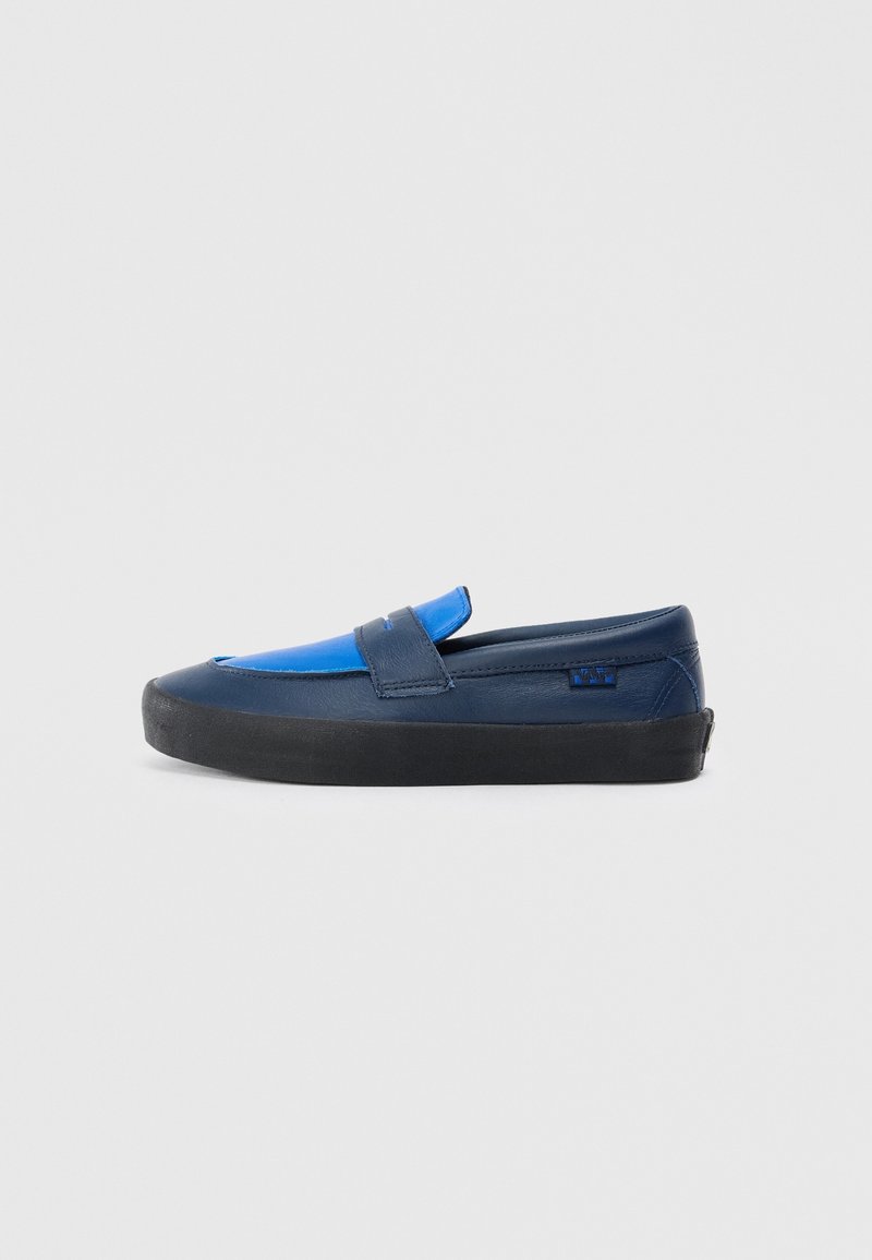 Chaussure mocassin homme à enfiler en cuir bleu foncé et bleu clair avec semelle en caoutchouc noire, vue de profil sur un fond gris clair uni.