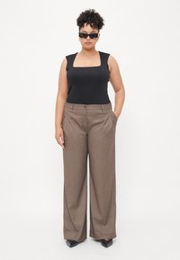 Black sleeveless bodysuit, brown wide-leg trousers with pockets, a button closure, and black pointed-toe shoes, modeled against a white background.