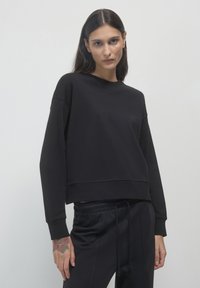 Felpa nera corta con scollo rotondo, spalle scese e maniche lunghe. Realizzata in tessuto morbido con una texture liscia.