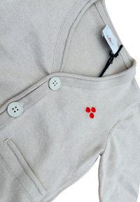 Cardigan color beige chiaro con scollo a V, dotato di due bottoni e un piccolo dettaglio ricamato rosso. Tessuto morbido, maglia leggera.