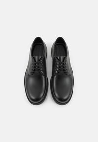 Chaussures en cuir noir avec une finition lisse, bout rond et design à lacets à cinq œillets. Semelle extérieure texturée avec un motif de traction subtil.