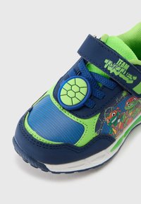 Pantofi sport pentru copii, albastri și verzi, cu partea superioară din plasă, închidere cu velcro, emblemă de broască țestoasă și un desen cu țestoase de desene animate pe lateral.