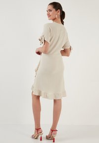 Beige dress with short, tied sleeves and a ruffled hem. Made of textured fabric, it features a fitted waist and flows loosely below.