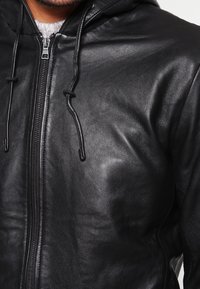 Zwarte leren hoodie met ritssluiting, capuchon met trekkoord en een gladde textuur. Heeft een getailleerd ontwerp en minimale hardware accenten.