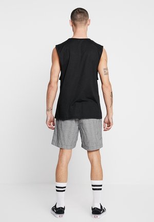 Chemise sans manches noire en coton, associée à un short à carreaux gris, des chaussettes blanches avec des rayures noires et des chaussures noires.