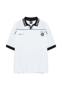 Polo blanc à manches courtes avec col et bordures de manches noirs, texte sur le col, petit texte sur la poitrine gauche, et un emblème circulaire avec trois étoiles sur la poitrine droite.
