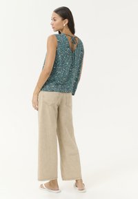 Haut sans manches à motif turquoise avec fermeture à nouer au dos, associé à un pantalon large beige et des sandales blanches.