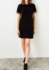 Černé bavlněné tričko šaty s krátkými rukávy a pruhovaným barevným lemem. Navrženo s volným střihem, sahající po polovinu stehen.