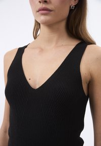 Top in maglia nera a coste con scollatura a V. Presenta linee verticali testurizzate e spalline larghe, silhouette aderente.