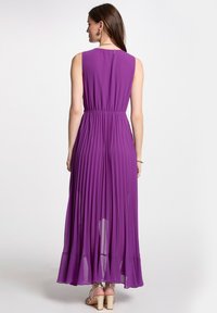 Robe maxi plissée violette avec un haut structuré, une taille élastique, une jupe fluide et un ourlet légèrement transparent. Vue de dos affichée.