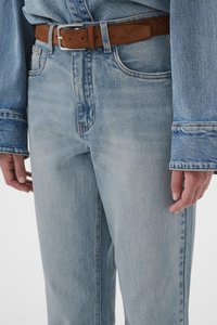 Svetlomodré rifle z denimu s vysokým pásom a priamym strihom, so subtílnym vyblednutím a hnedým semišovým opaskom. Výrazné šitie ako detail.