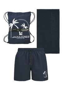 Shorts de bain bleu marine, sac à dos à cordon assorti avec imprimé palmiers blancs, et serviette bleu marine foncé embossée du nom de la marque.