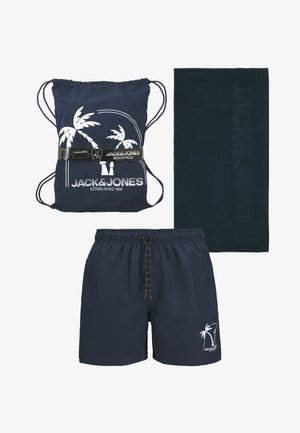 Dunkelblaue Badeshorts, passender Rucksack mit Kordelzug im weißen Palmen-Design und dunkelblauem Handtuch, das mit dem Markennamen geprägt ist.