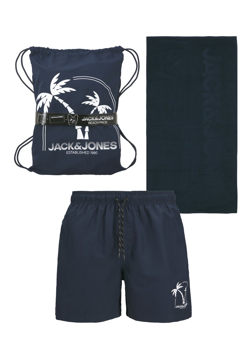 Shorts de bain bleu marine, sac à dos à cordon assorti avec imprimé palmiers blancs, et serviette bleu marine foncé embossée du nom de la marque.